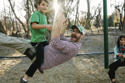 Portrait of happy family swinging against bare trees in playground