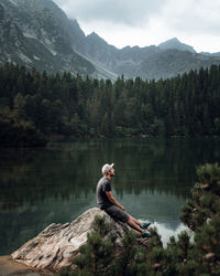 Rear view of man sitting on rock by lake