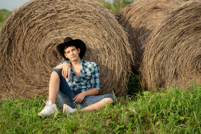 Full length of young man sitting on field near the haystack 