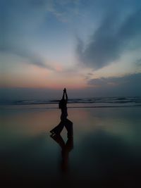 Silhouette man standing in sea against sky during sunset