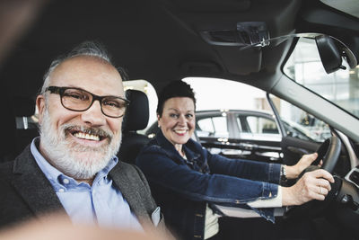 Portrait of happy senior man and woman sitting in car at showroom