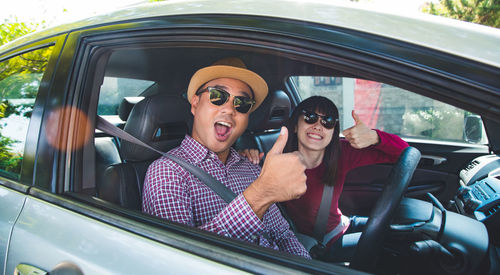 Portrait of couple showing thumbs up while sitting in car