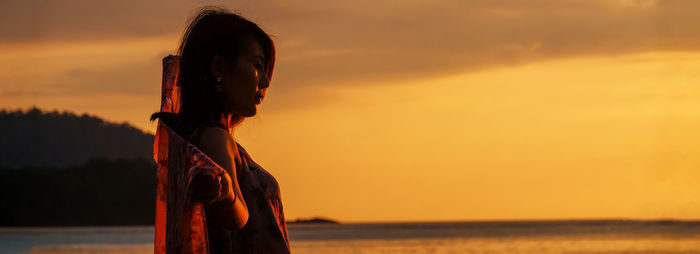 Woman looking at sea against sky during sunset