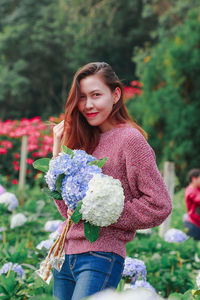 Portrait of beautiful young woman standing by flowering plants