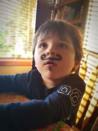 Cute boy with face paint looking away while sitting by table at home