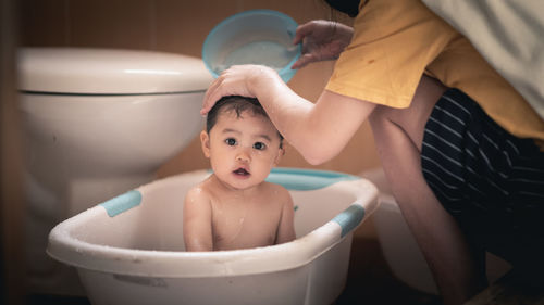 Midsection of mother bathing baby daughter in bathroom