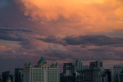 Buildings in city against dramatic sky during sunset