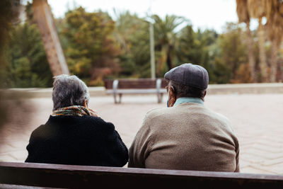 Back view of an unrecognizable elderly couple sitting on a park bench