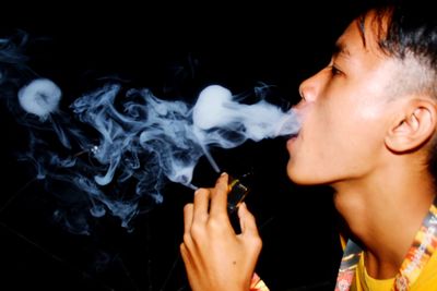 Midsection of man smoking cigarette against black background