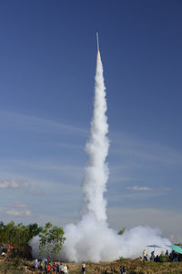 Rocket taking off from field against sky