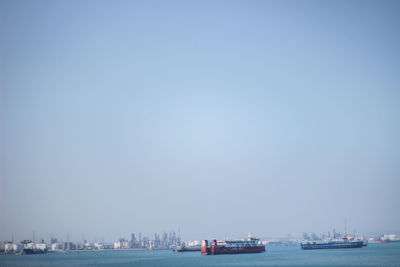 Boats in sea against clear blue sky