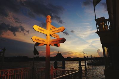 Road sign by city against sky during sunset