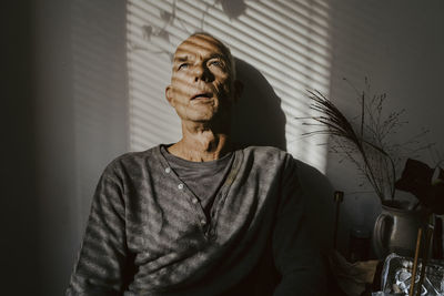 Depressed senior man against wall at home