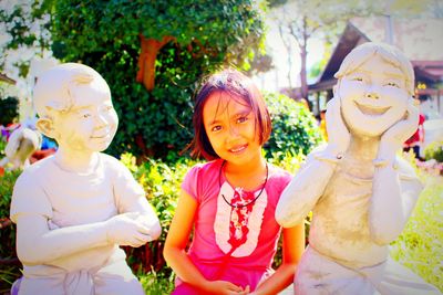 Portrait of smiling girl sitting by statues at park