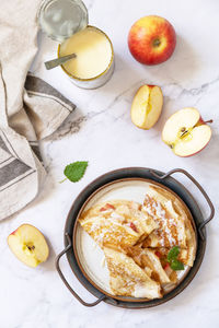Homemade sweet crepes with apples and condensed milk on a marble tabletop. top view flat lay.