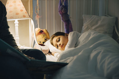 Cropped image of father reading book to daughter sleeping in bed at home