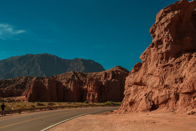 Road leading towards mountains against blue sky