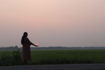 Side view of woman standing on field against clear sky