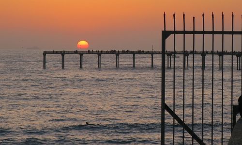 Wooden post in sea against sky during sunset