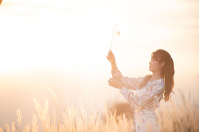 Side view of woman standing on field against sky during sunset