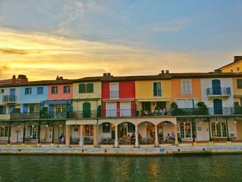 Buildings by river against sky during sunset