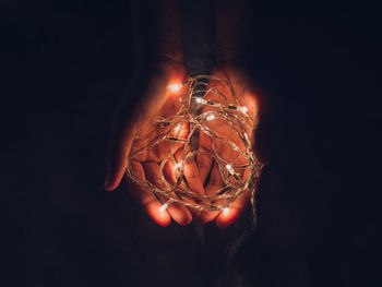 Cropped hands of person holding illuminated string lights against black background