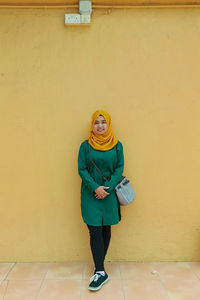 Portrait of smiling young woman standing against yellow wall