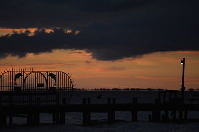 Silhouette built structure by sea against sky during sunset