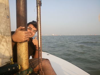 Portrait of young man gesturing thumbs up while sitting in sailboat over sea