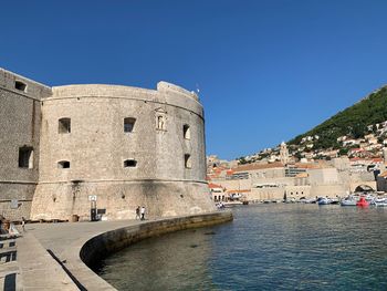 Historic building by sea against clear blue sky