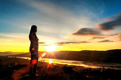 Side view of silhouette woman standing against mountains during sunset