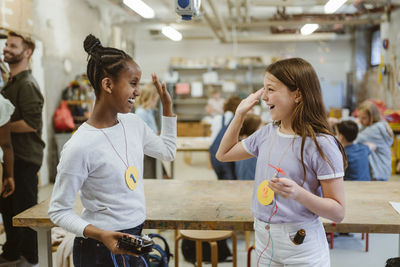 Cheerful female students giving high-five while standing near table in classroom