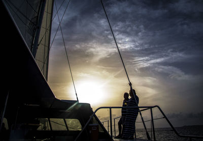 Silhouette man standing on sailboat against sky during sunset