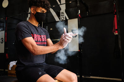 Young man wearing mask sitting at gym