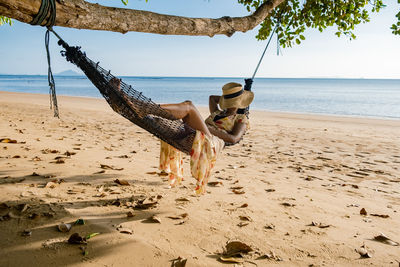 Full length of woman relaxing on hammock at beach