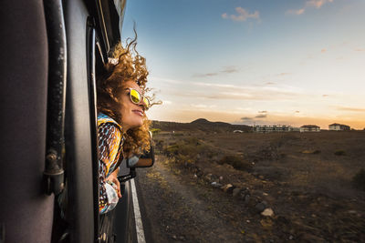 Woman looking away through car window against sky