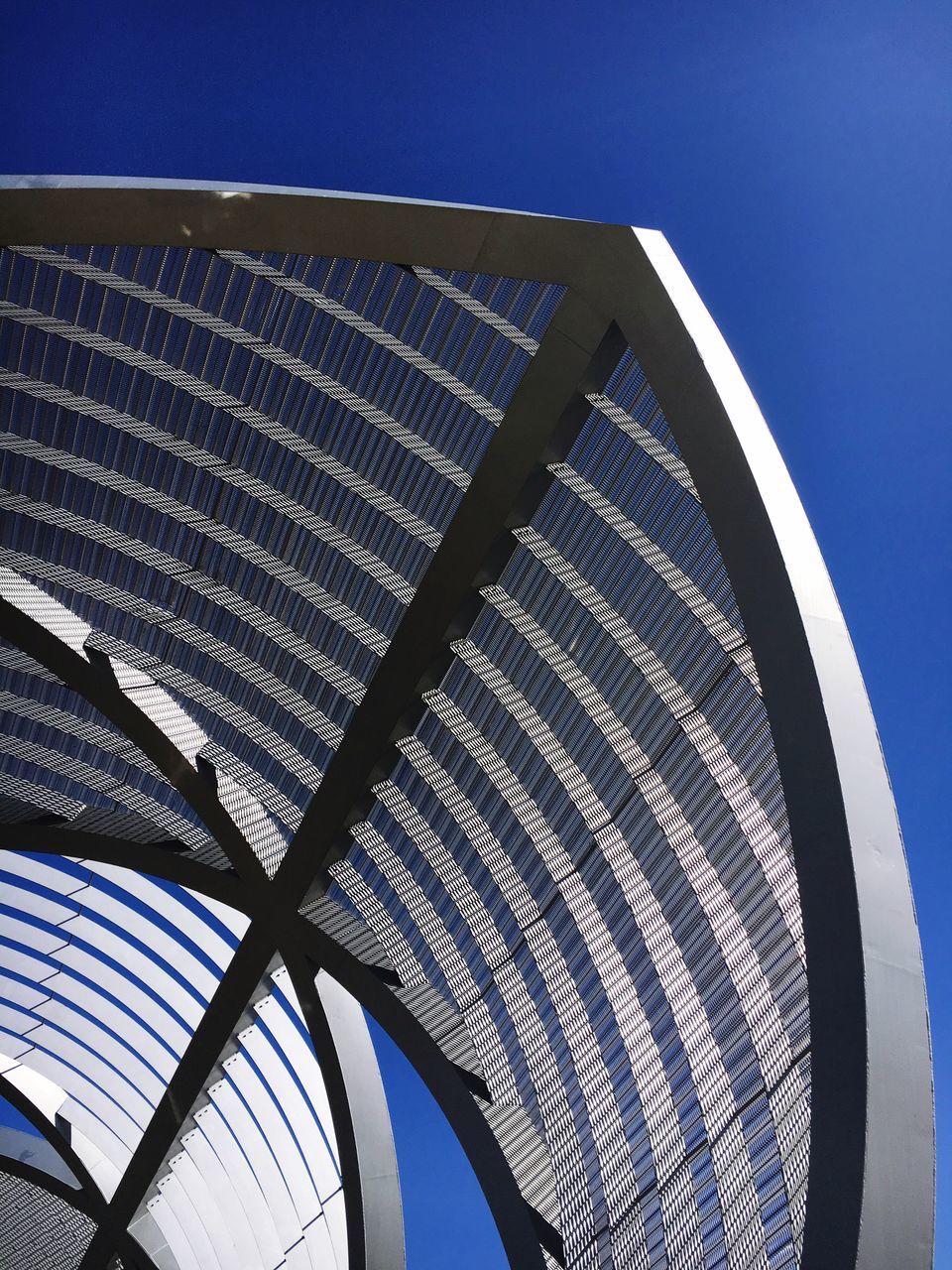 clear sky, blue, low angle view, pattern, built structure, metal, sky, sunlight, architecture, no people, day, metallic, outdoors, arts culture and entertainment, design, modern, ferris wheel, part of, copy space, nature