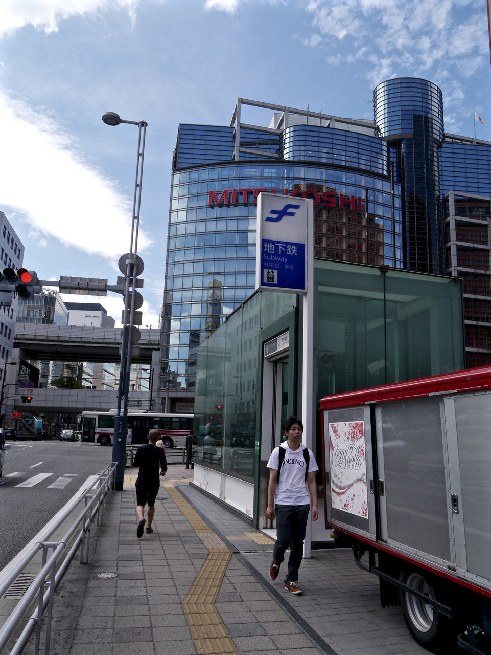 architecture, building exterior, built structure, city, person, city life, men, tower, lifestyles, street light, office building, sky, tall - high, development, skyscraper, casual clothing, group of people, day, outdoors, footpath