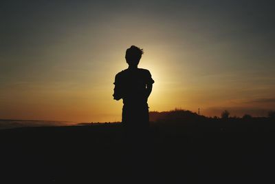 Silhouette statue on field against sky during sunset