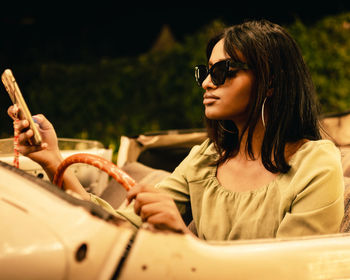 Portrait of young woman in sunglasses using her phone in a convertable car