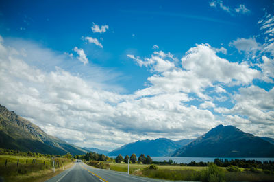 Country road leading towards mountains against sky