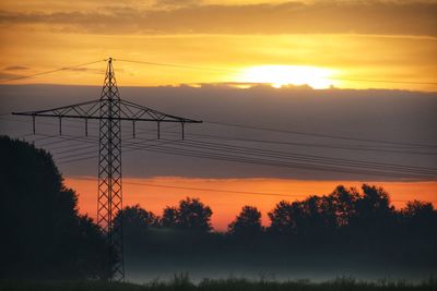 Silhouette trees and electricity pylon against romantic sky at sunset