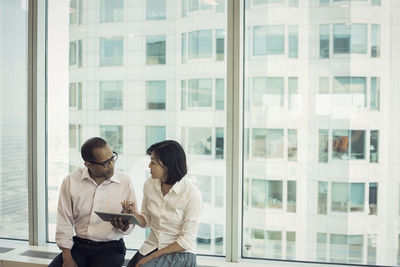 Business people with digital tablet sitting on window sill, discussing