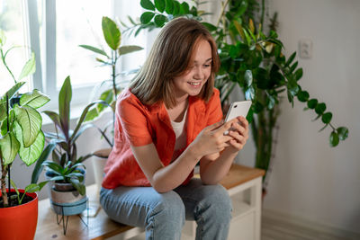Smiling young woman using mobile phone while sitting at home