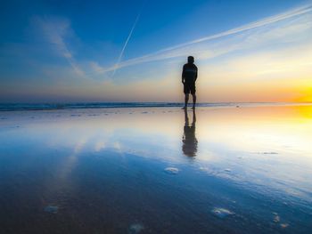 Rear view of silhouette man standing at beach during sunset