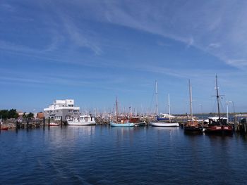 Sailboats moored at harbor against blue sky