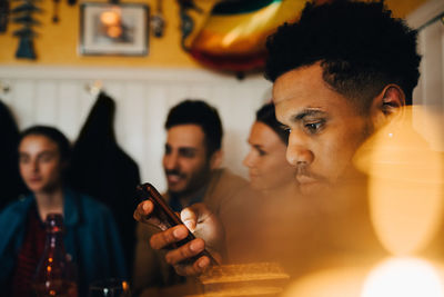 Young man using smart phone while sitting by friends at restaurant during dinner party