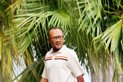 Mature man standing against palm tree
