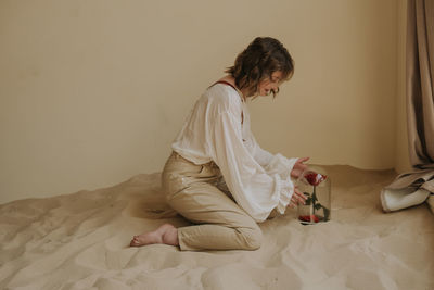 Young female in victorian shirt sitting with rose on the sand and smile