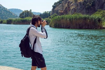 Man in a shirt and shorts photographs on camera the river and the mountain in dalyan